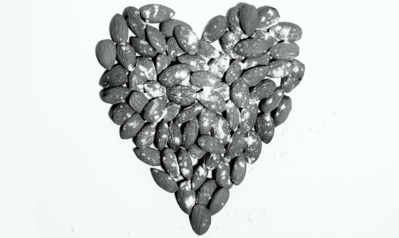 Black and white photo of almonds arranged in a heart shape on a white surface.