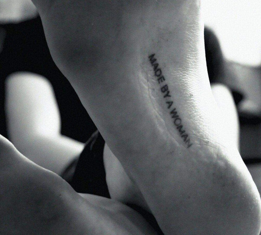 Black and white close-up photo of a tattoo that reads "Made by a woman."