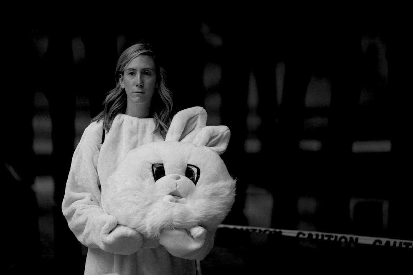 Black and white portrait of Laura wearing a bunny suit, holding the head of the costume in her arms.