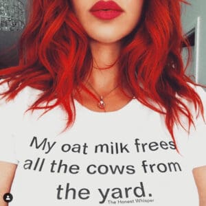 Close-up photo of a woman wearing a white t-shirt with the message "My oat milk frees all the cows from the yard." printed on it.