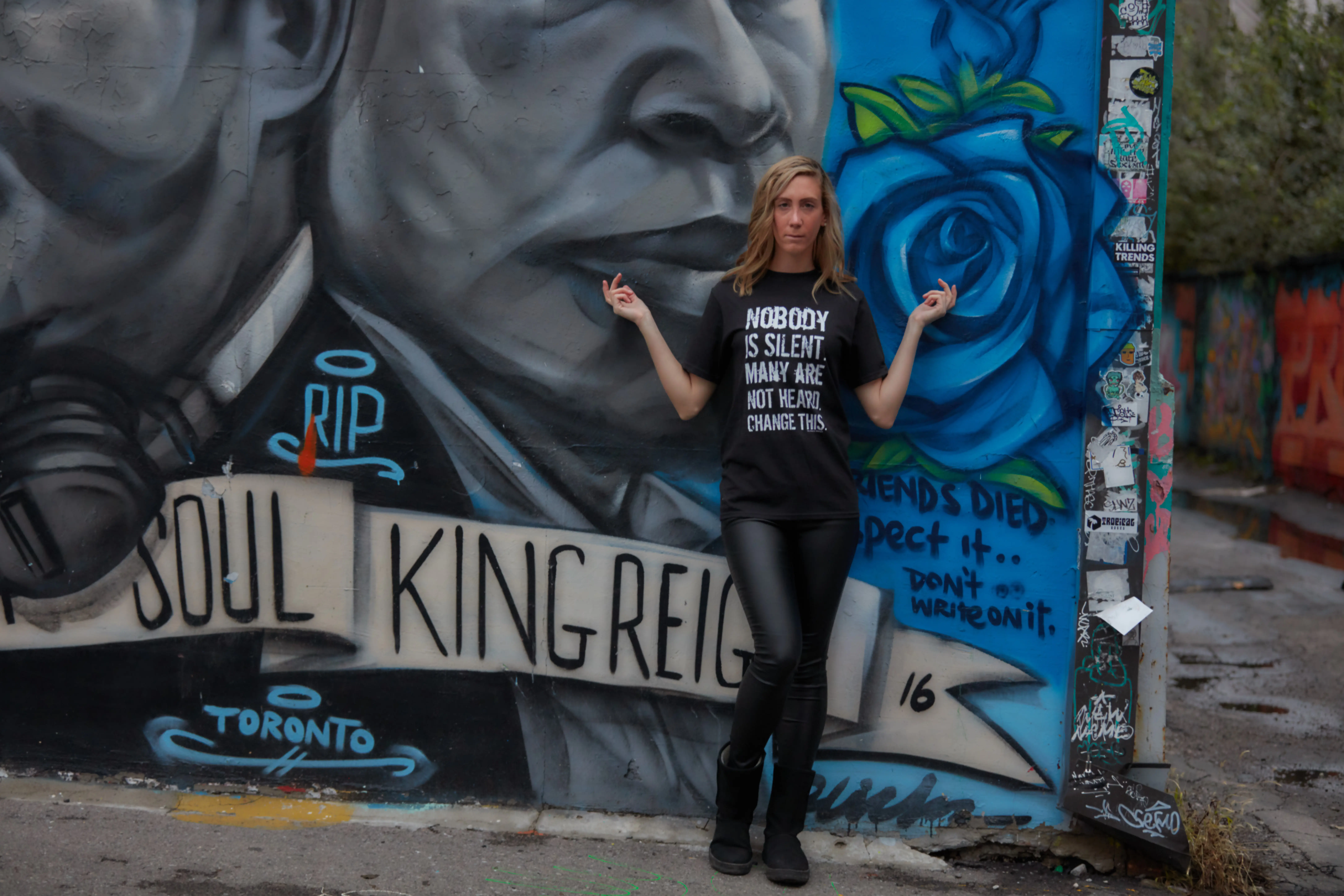 Laura posing in front of a graffiti wall wearing a t-shirt from The Honest Whisper with the message 