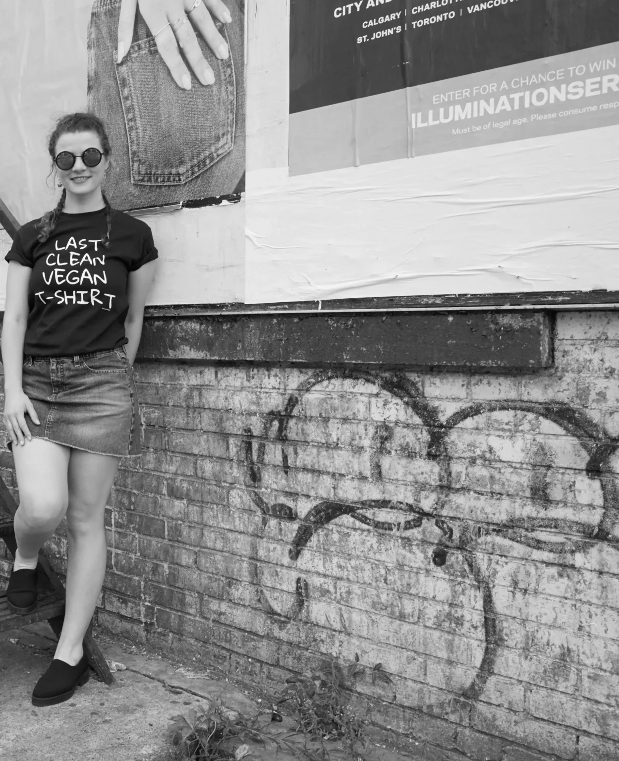 A woman leaning against a brick wall wearing a white t-shirt with the message 