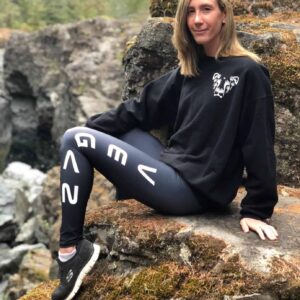 Laura sitting on a rock formation wearing a crew sweater with the Dandi Lion logo and vegan tights, both from The Honest Whisper