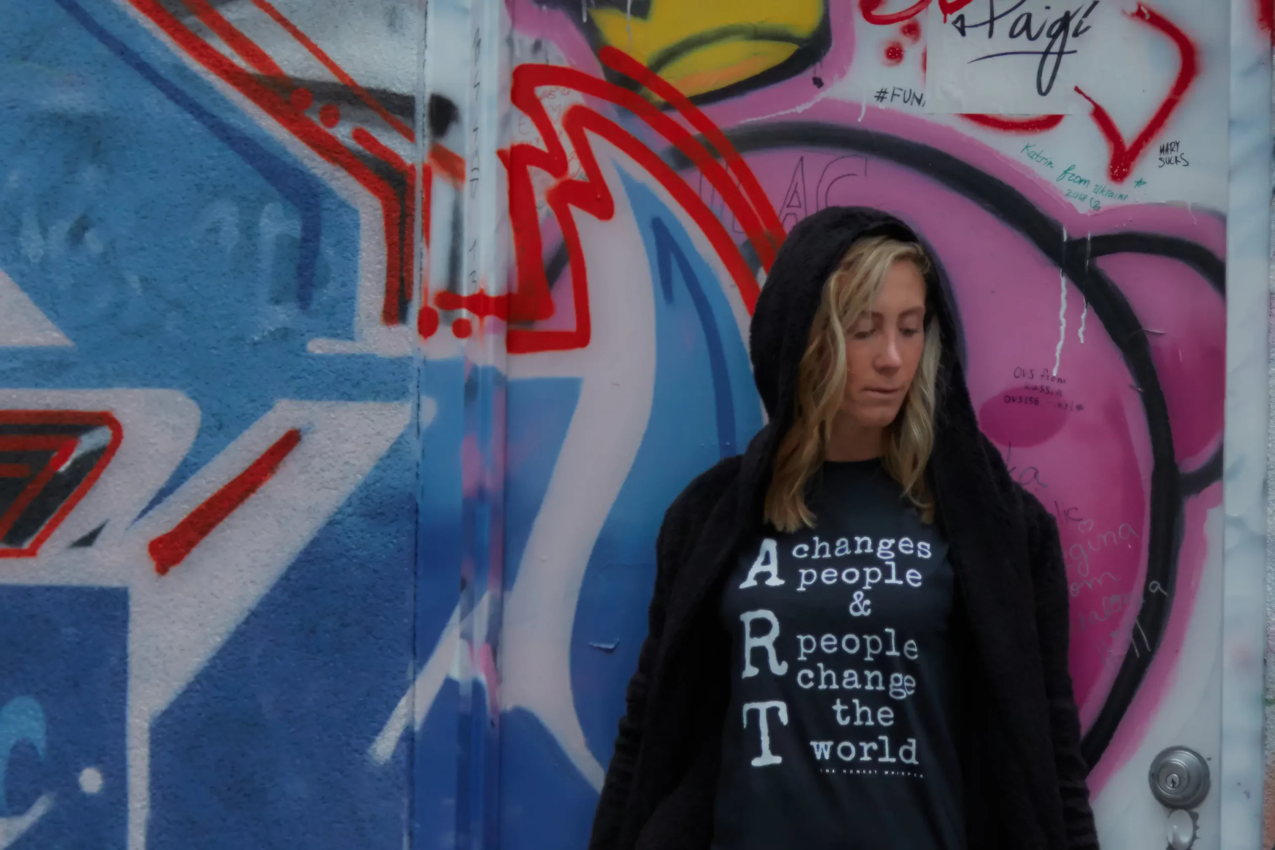 Laura posing in front of a graffiti wall wearing a t-shirt from The Honest Whisper with the phrase 