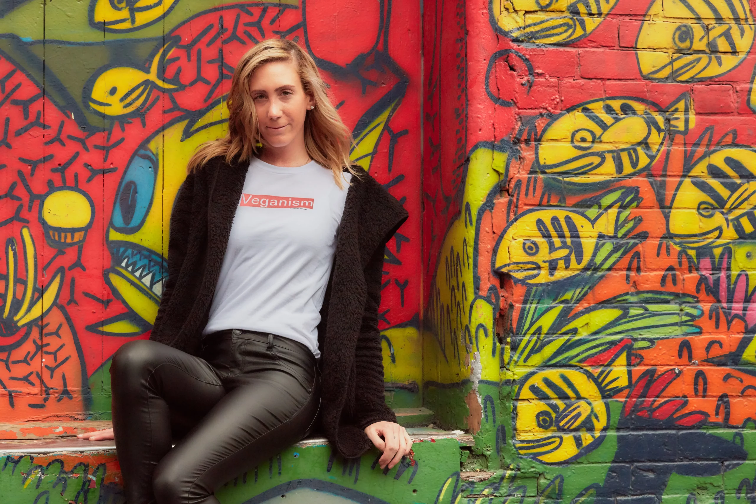 Laura posing in front of a graffiti wall wearing a t-shirt from The Honest Whisper with the word 