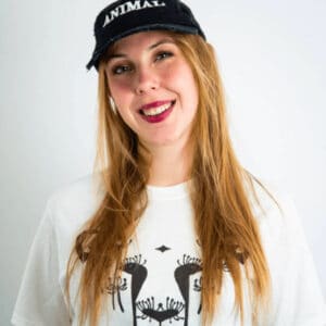 A woman wearing a white T-shirt with the DandiLion logo of The Honest Whisper, an ethical and sustainable fashion brand, and a hat that says "ANIMAL"