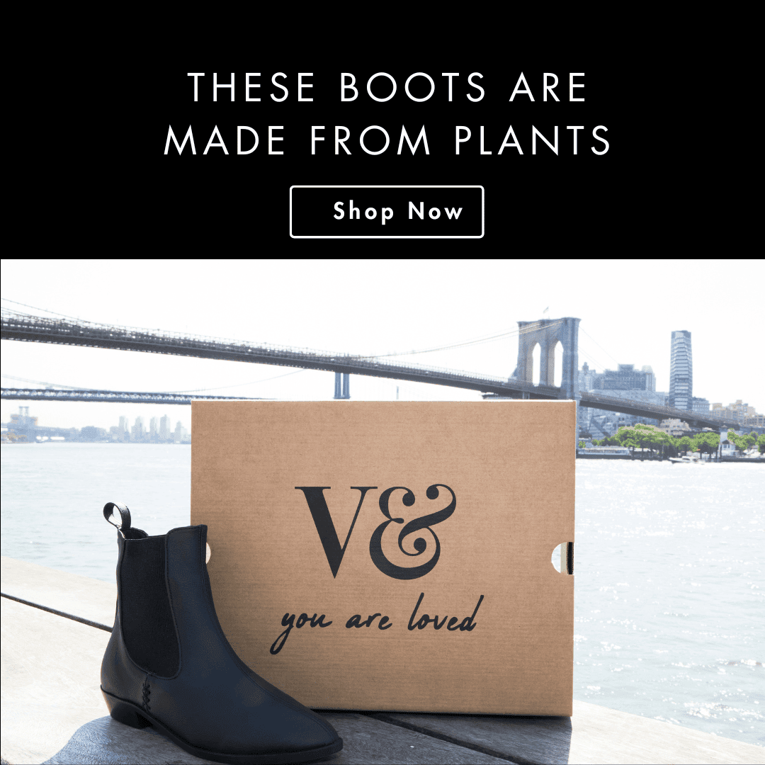 A pair of black vegan leather Chelsea boots from V&Co sitting on a box with the brand logo and the phrase "you are loved" written on it. The Brooklyn Bridge is in the background.