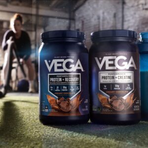 A side-by-side comparison of Vega Protein plus Recovery and Vega Protein plus Creatine tubs with a Vega shaker bottle in a gym setting.