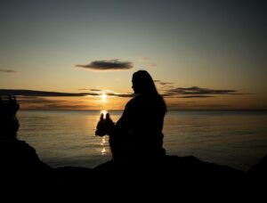 Sunset over water with a woman holding a cat, creating a peaceful and calming scene.